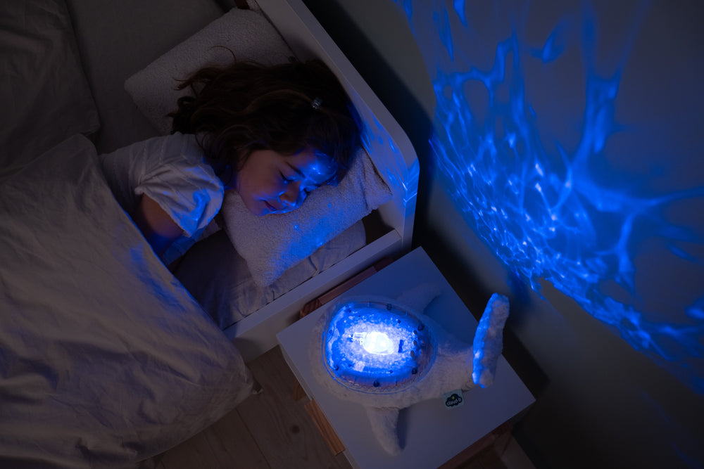 Child lying in bed with a glowing blue night light on a nightstand.