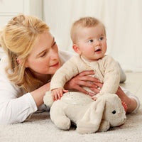 Woman holding a baby with a plush toy on a carpeted floor